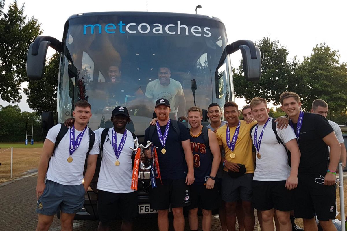 The Saracens team in front of a MET Coaches coach, happy, celebrating their win at the Premiership Rugby 7s